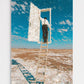 Person on a ladder opening a door in a desert landscape with a blue sky.