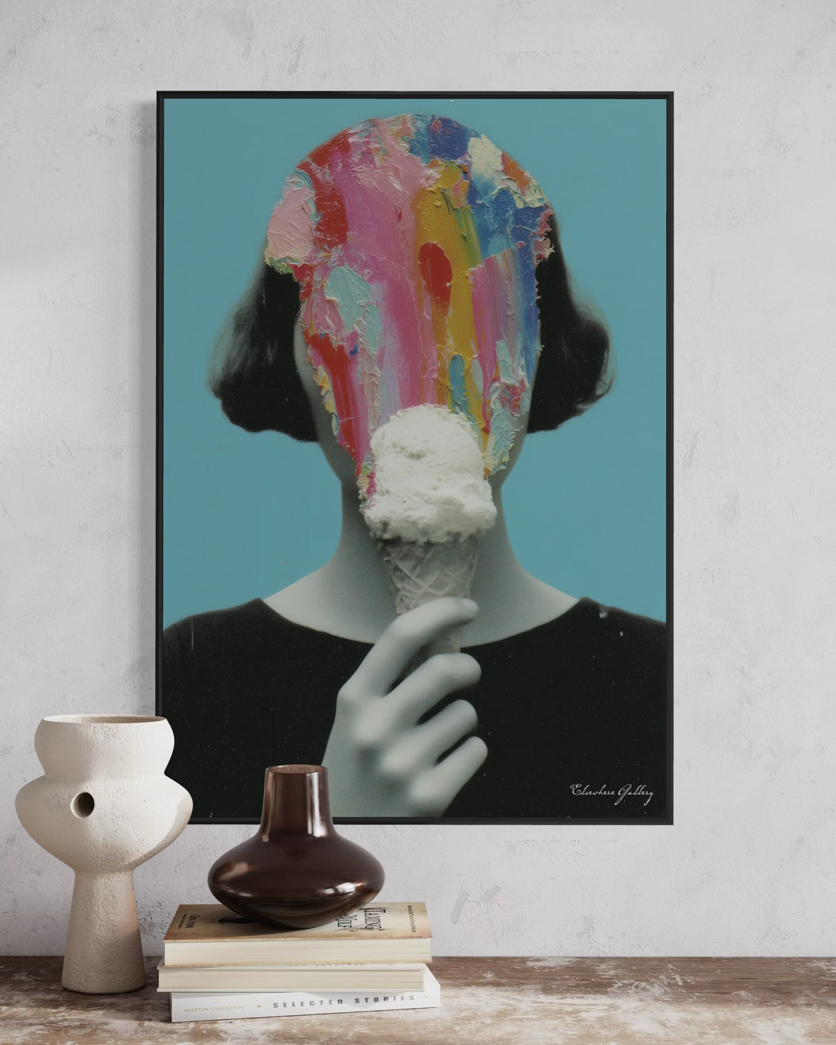 Framed abstract art print of a colorful head on a white wall with decorative vases and books below.