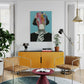 Modern living room with yellow cabinet, brown chairs, and colorful artwork on the wall.