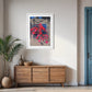 Framed artwork on a wall above a wooden sideboard in a room with a plant and blue door.