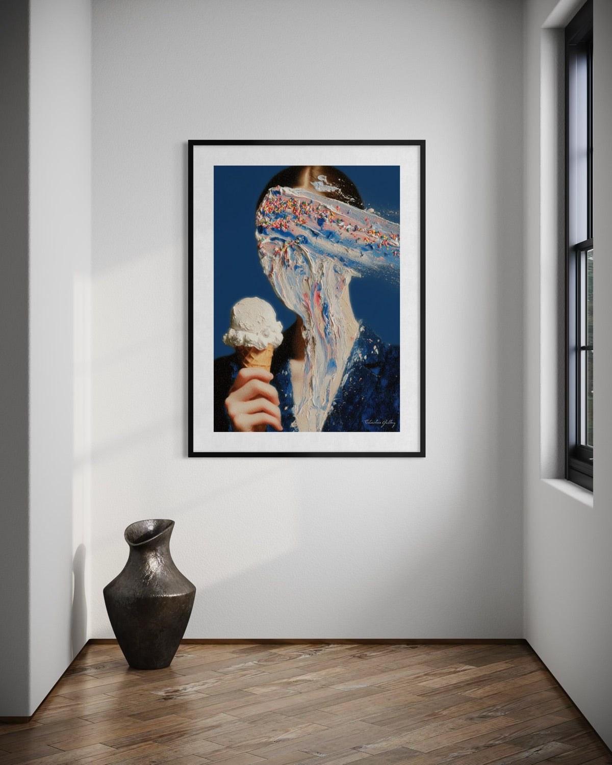 Framed artwork of a person with ice cream on a wall in a room with a vase on the floor.