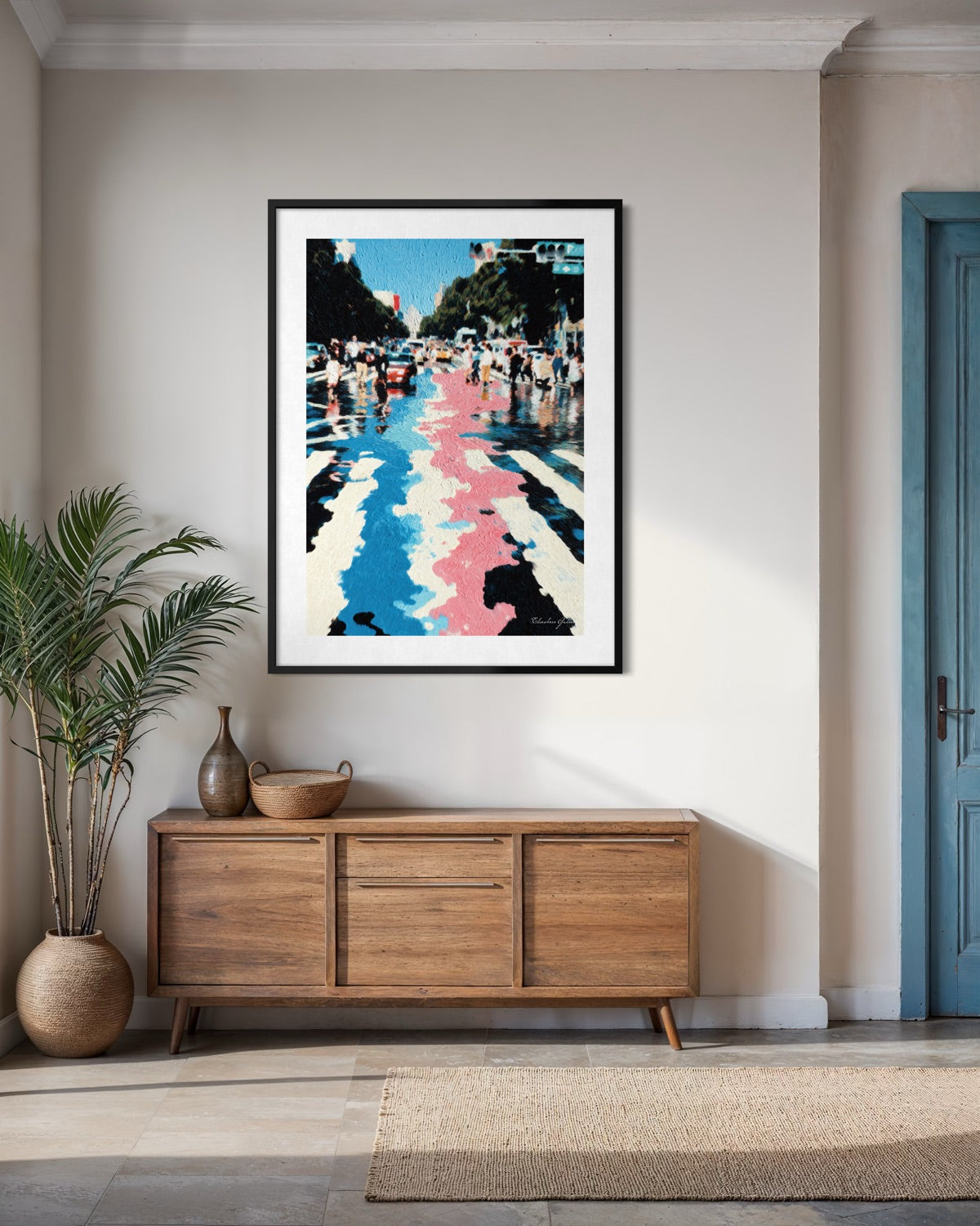 Framed artwork on a wall above a wooden sideboard in a room with a plant and door.
