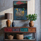 Decorative console table with vases, a lamp, and a painting on a textured wall.