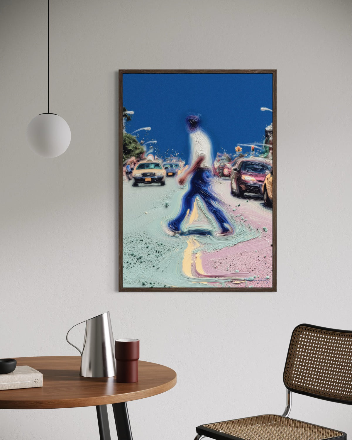 Framed artwork of a person walking on a street with cars in an urban setting, displayed in a room with a table and chair.