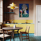 Modern kitchen with yellow cabinets, wooden table, and colorful wall art.