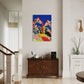 Colorful abstract painting of giraffes on a wall above a wooden cabinet in a room with a staircase.