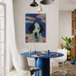 Dining room with a blue table and white chairs, featuring a colorful painting of a dog on the wall.