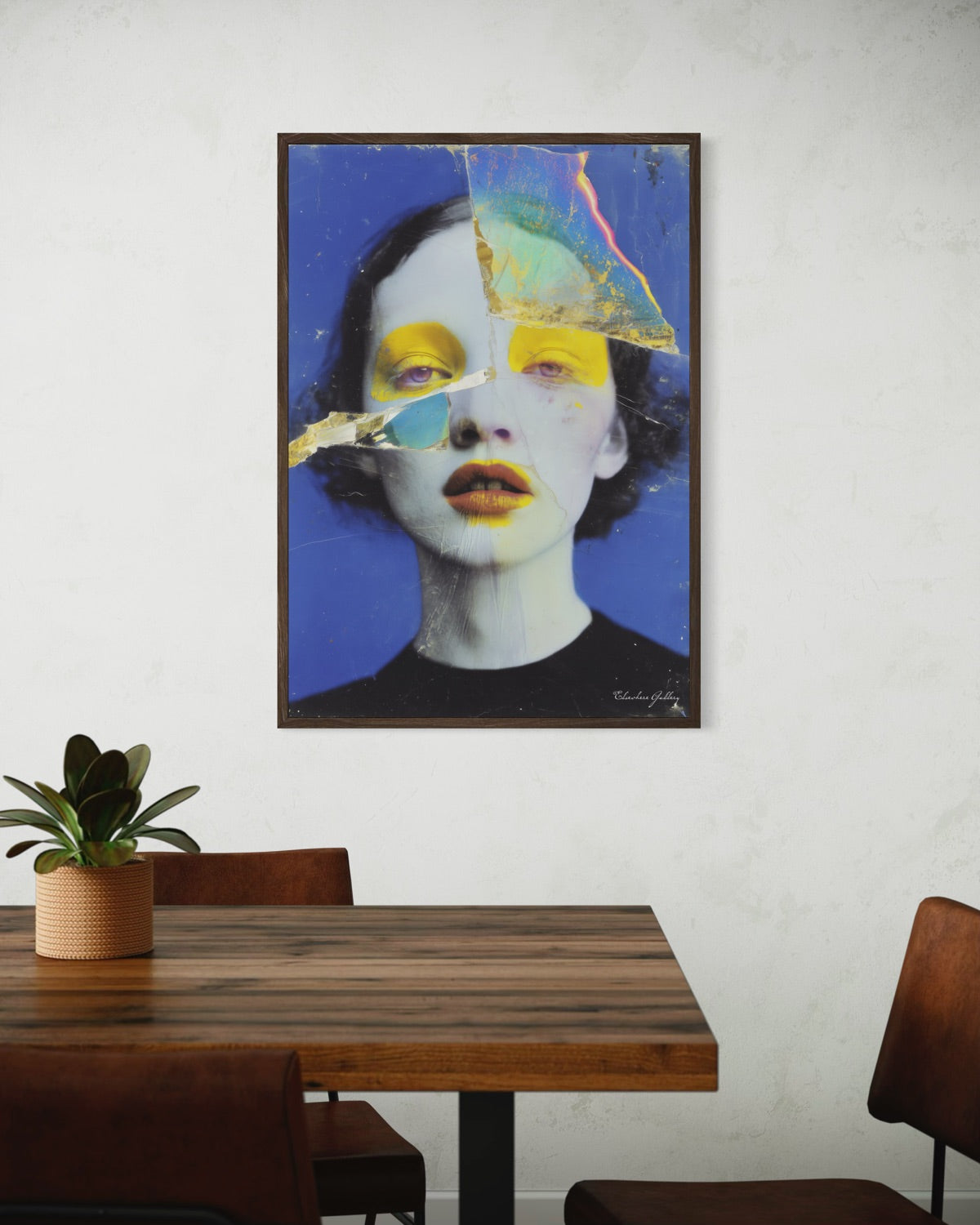 Framed abstract art of a face on a wall above a wooden table with chairs.