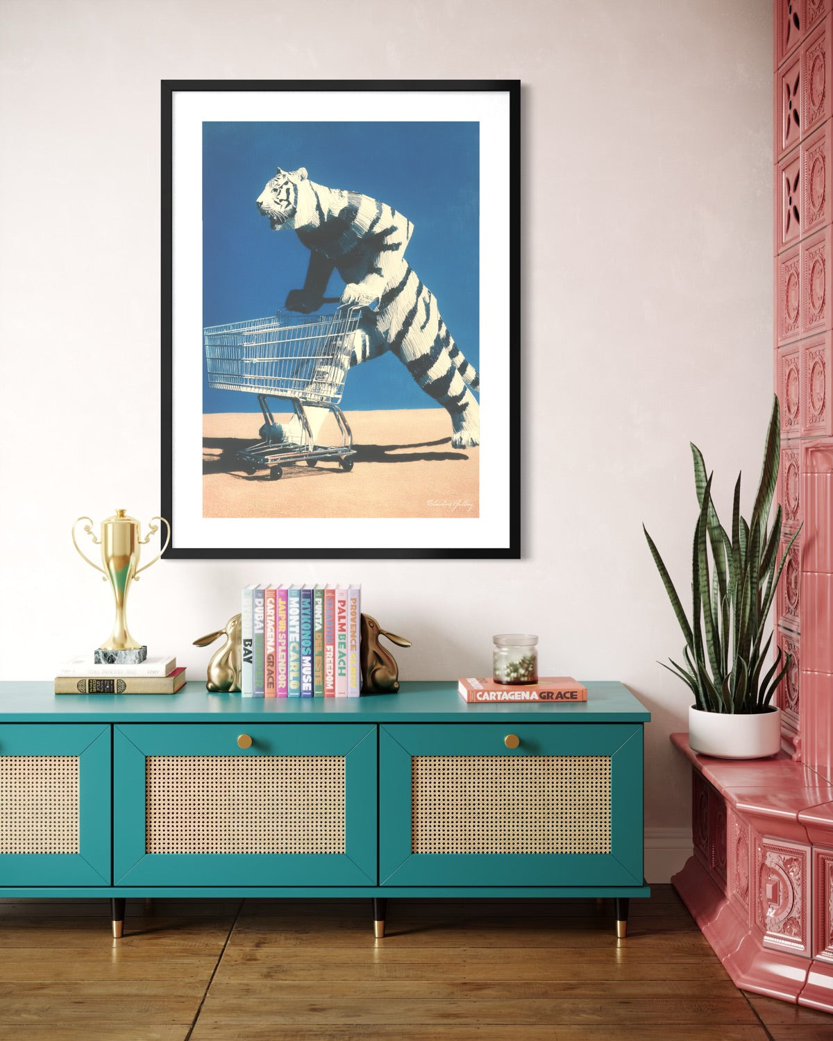 Framed artwork of a tiger pushing a shopping cart on a teal console table with decorative items.