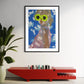 Framed artwork of a person wearing sunglasses with a blue sky background, placed on a red console table.