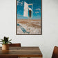 Framed artwork of a person on a ladder against a blue sky with clouds, displayed above a wooden table.