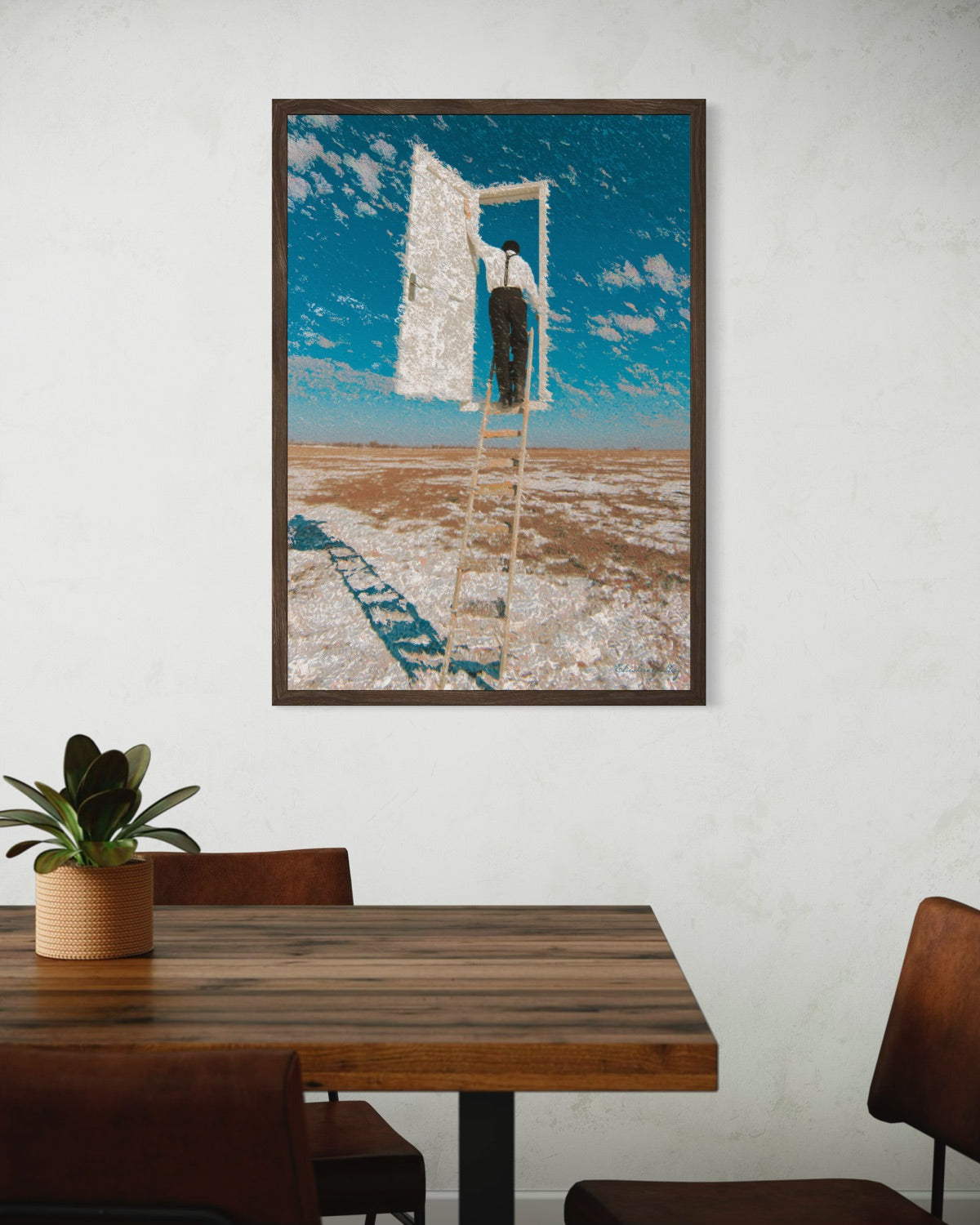 Framed artwork of a person on a ladder against a blue sky with clouds, displayed above a wooden table.