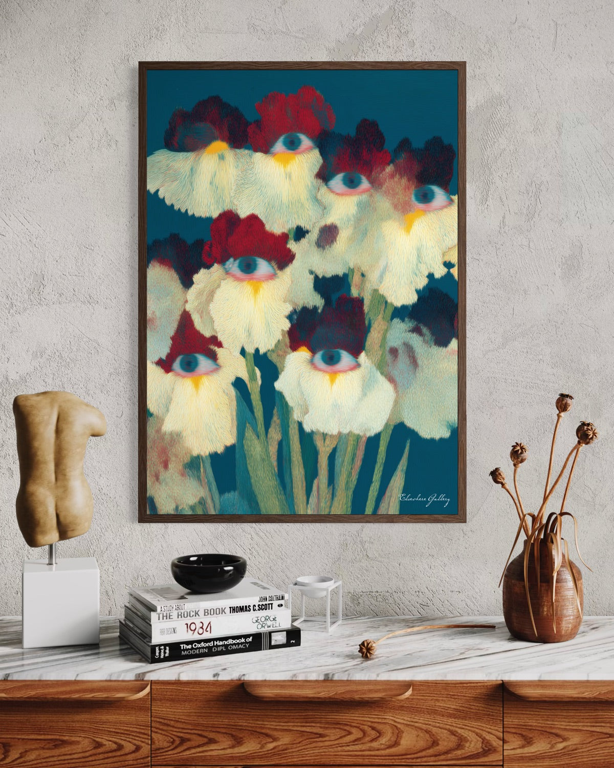 Framed abstract artwork of flowers with blue eyes on a wall above a wooden cabinet.