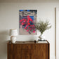 Wooden sideboard with a lamp, books, and a vase against a wall with a colorful abstract painting.