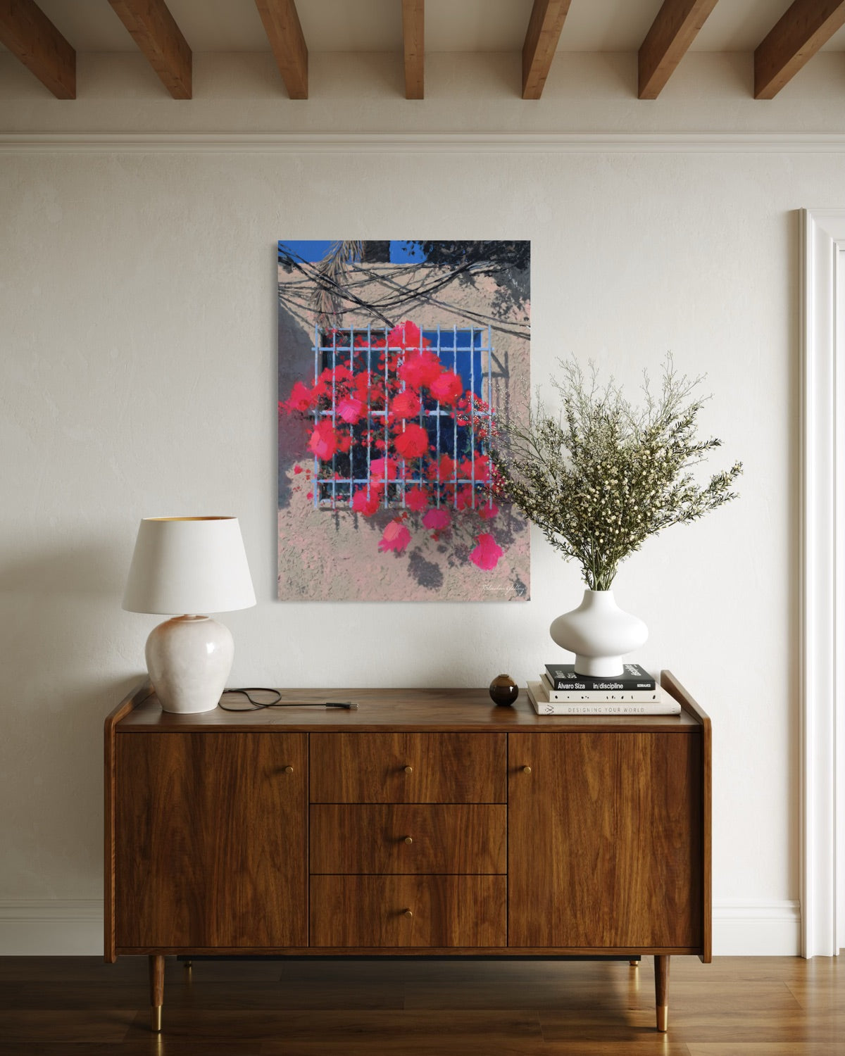 Wooden sideboard with a lamp, books, and a vase against a wall with a colorful abstract painting.