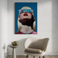 Framed artwork of a stylized portrait on a wall above a chair and small table.