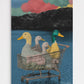 Surreal contemporary pop art print featuring four colorful ducks sitting inside a metal shopping cart floating on a blue lake, set against monochromatic mountains and vibrant sunset clouds, titled "Lost In The Ducks."